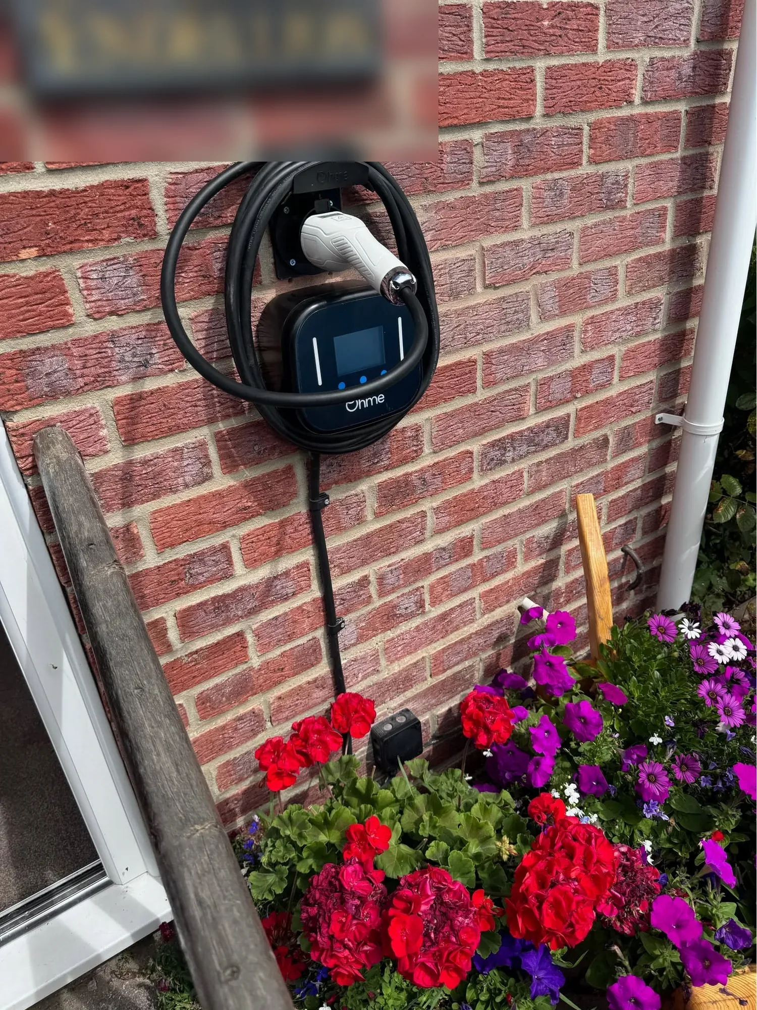 Ohme electric vehicle charger installed on a brick wall beside a front door