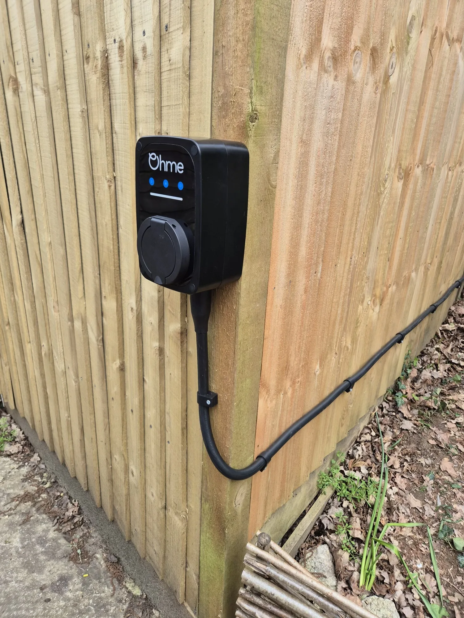 Ohme home EV charger installed on a timber garden fence
